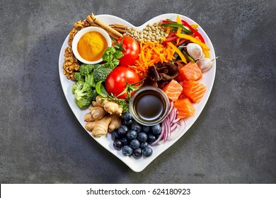 Healthy diet for the cardiovascular system with a heart-shaped plate of acai, lentils, soy sauce, ginger, salmon, carrot, tomato, turmeric, cinnamon, walnuts, garlic, peppers, broccoli, basil, onion