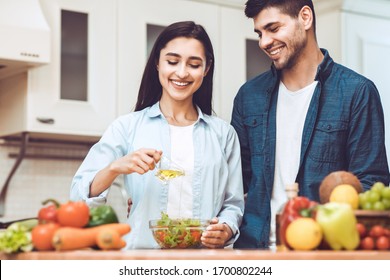 Healthy Diet Concept. Lovely couple preparing dinner at kitchen, girl pouring olive oil into bowl of salad, selective focus