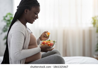 Healthy Diet During Pregnancy. Black Expectant Woman Eating Fresh Vegetable Salat At Home, Happy Pregnant African Lady Enjoying Tasty Organic Food While Relaxing On Bed, Side View With Free Space