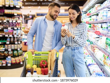 Healthy Diet And Lifestyle. Happy Couple Doing Shopping Standing In Supermarket With Trolley Cart, Buying Food, Choosing Products, Holding And Looking At Bottle Of Milk Near Shelves With Dairy - Powered by Shutterstock