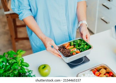Healthy diet plan for weight loss, daily ready meal menu. Close up Woman weighing lunch box cooked in advance,ready to eat on kitchen scale. Balanced portion with healthy dish. Pre-cooking concept