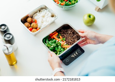 Healthy diet plan for weight loss, daily ready meal menu. Close up Woman weighing lunch box cooked in advance,ready to eat on kitchen scale. Balanced portion with healthy dish. Pre-cooking concept - Shutterstock ID 2172181813