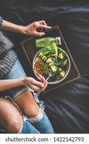 Healthy Dinner, Lunch In Bed. Vegan Superbowl Or Buddha Bowl With Hummus, Vegetable, Salad, Beans, Couscous And Avocado, Green Smoothie On Tray And Woman In Warm Sweater Eating With Fork, Top View