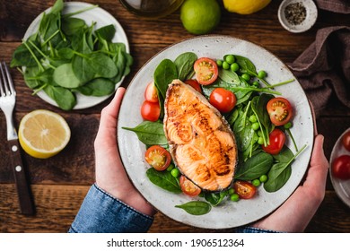 Healthy Dinner Meal With Roasted Salmon Steak, Baby Spinach And Cherry Tomatoes Salad. Male Hands Holding Plate With Healthy Food