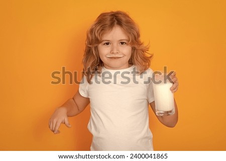 Healthy drink with calcium and protein for kids. Child with a glass of milk on studio background. Cute boy in white shirt holding glass of milk on isolated on yellow. Kid with milk mustache.