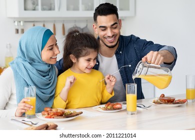 Healthy Drink. Happy Arab Father Pouring Orange Juice For His Daughter And Wife While They Having Breakfast Together In Kitchen, Cheerful Muslim Family Smiling And Enjoying Time Together At Home - Powered by Shutterstock