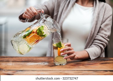 Healthy drink for healthy life. Close-up of young woman pouring fresh lemonade to glass while standing at the wooden desk