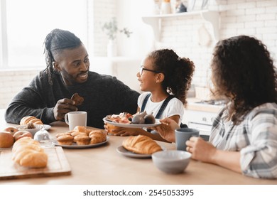 Healthy eating. African-american family, parents and daughter having morning breakfast at home kitchen, talking and spending time together. Family bonding - Powered by Shutterstock