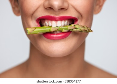 Healthy Eating. Closeup Of Woman Mouth With Beautiful Pink Lips Makeup Holding Fresh Asparagus Between White Teeth. Smiling Female Face With Vegetable In Mouth. Diet Food Concept. High Resolution