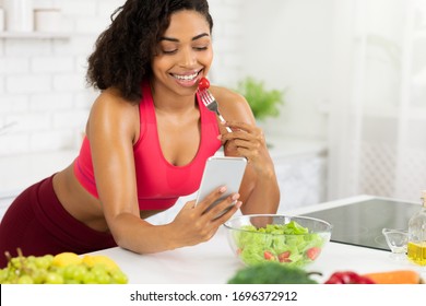 Healthy Eating Concept. Beautiful black woman eating salad using application, sending message on smartphone device - Shutterstock ID 1696372912