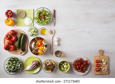 Healthy eating concept with fresh vegetables and salad bowls on kitchen wooden worktop, copy space at right, top view