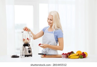 Healthy Eating, Cooking, Vegetarian Food, Dieting And People Concept - Smiling Young Woman Putting Fruits And Berries For Fruit Shake To Blender Shaker At Home