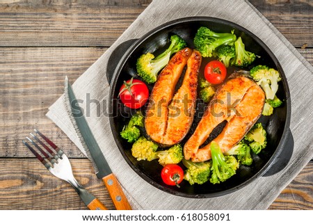 Healthy eating, diet. Baked grilled trout (salmon) with vegetable garnish - broccoli, tomatoes. In a portioned frying pan, on a wooden table. Top view copy space 