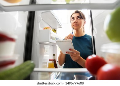 healthy eating and diet concept - woman opening fridge and making list of necessary food at home kitchen - Powered by Shutterstock