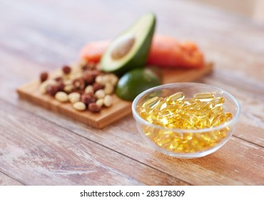 healthy eating, diet and omega 3 nutritional supplements concept - close up of cold liver oil capsules in glass bowl and food on table - Shutterstock ID 283178309