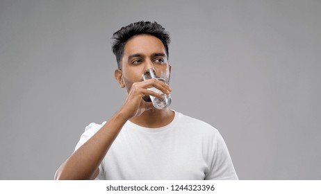 healthy eating, diet and people concept - happy young indian man drinking water from glass over grey background