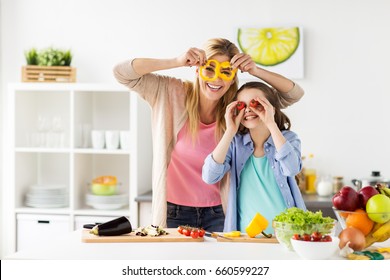 Healthy Eating, Family And People Concept - Happy Mother And Daughter Cooking Vegetables For Dinner And Having Fun At Home Kitchen