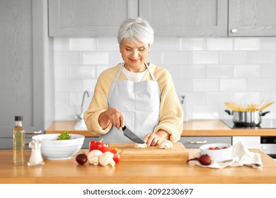 healthy eating, food cooking and culinary concept - happy smiling senior woman with knife chopping champignons on kitchen at home - Powered by Shutterstock