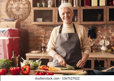 Healthy eating habits. Cheerful senior woman cutting vegetables for salad, cooking in kitchen, free space - Powered by Shutterstock