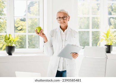 Healthy eating habits. Dietitian doctor nutritionist showing green apple for balanced diet for weight loss at hospital holding digital tablet.