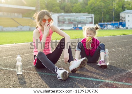 Healthy eating and healthy lifestyle in children, girl teenager and girl 7 years after playing sports sitting in the stadium drinking water and eating apples.