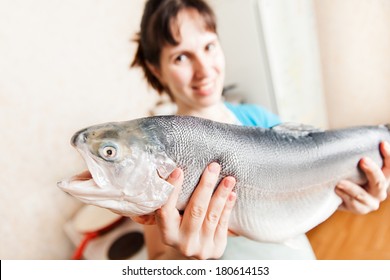 Healthy eating seafood - beauty young smiling woman hand holding raw salmon or trout fish food at kitchen