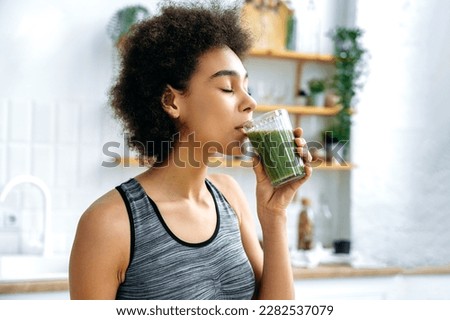 Healthy eating, veganism, raw food. Satisfied happy healthy african american young woman, stand in the kitchen, drinking healthy fortified organic smoothie from a glass cup, taking care of health