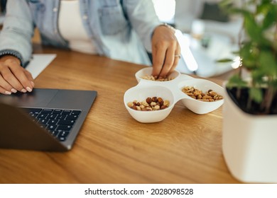 Healthy eating and working. Woman eating nuts while working on laptop. Close-up.