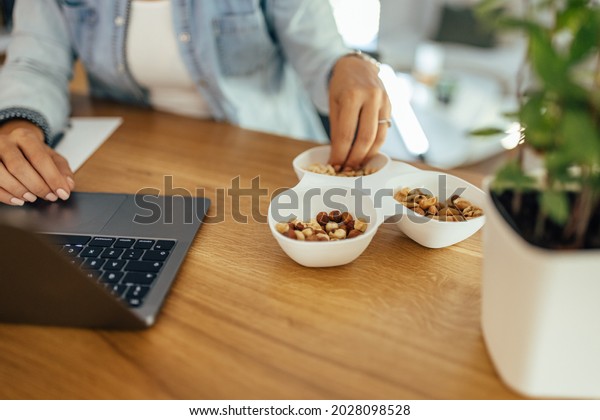 Healthy eating and working. Woman eating nuts\
while working on laptop.\
Close-up.