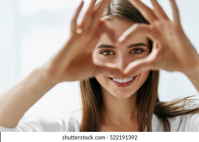 Healthy Eyes And Vision. Portrait Of Beautiful Happy Woman Holding Heart Shaped Hands Near Eyes. Closeup Of Smiling Girl With Healthy Skin Showing Love Sign. Eyecare. High Resolution Image