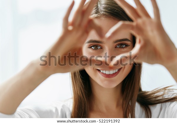 Healthy\
Eyes And Vision. Portrait Of Beautiful Happy Woman Holding Heart\
Shaped Hands Near Eyes. Closeup Of Smiling Girl With Healthy Skin\
Showing Love Sign. Eyecare. High Resolution\
Image