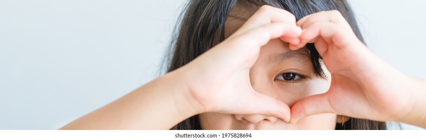 Healthy eyes and vision.asian kid child holding heart shaped hands on eyes. Love Sign for foster family adoption child.Eye care.beta Carotene vitamin.Focus, optician doctor, optical.Myopia, Love care. - Shutterstock ID 1975828694