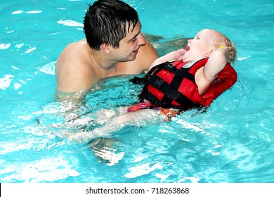 Healthy Family Father Teaching Baby Swimming Pool. The Little Blond Boy Learns To Swim In The Life Jacket. Dad Carefully And Fun Teaches The Child To Swim