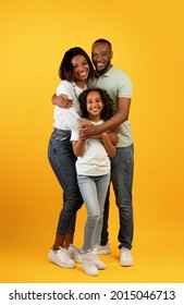 Healthy Family Relationship. African American Dad And Mom Embracing Smiling Daughter Standing Over Yellow Studio Background, Crop. Full Length Portrait