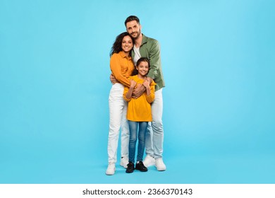 Healthy family relationship. European dad and mom embracing daughter, posing standing over blue studio background, full length portrait, free space - Powered by Shutterstock