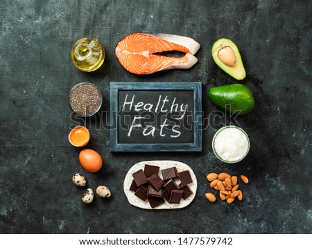 Healthy fats sources concept. Different food ingredients and chalkboard with ealthy Fats words on dark background. Top view or flat lay.