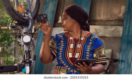 Healthy female cyclist holding digital device with instructions for bicycle repair. Athletic black woman using phone tablet for research on bike adjustments for maintenance at home yard. - Powered by Shutterstock