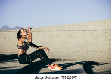 Healthy Female Sitting Outdoors And Drinking Water After Exercising Session. Fitness Woman Taking A Break After Workout.