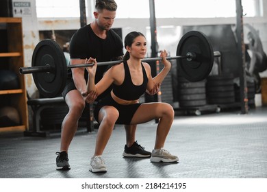 Healthy, Fit And Active Woman Exercising, Weight Training And Squatting With Her Fitness And Personal Trainer At The Gym. Athletic Young Female Athlete Lifting A Barbell With Her Bodybuilder Coach