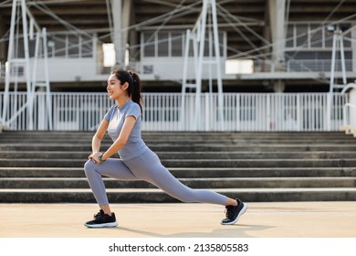 Healthy And Fit Asian Woman Wearing Sportswear Warming Up In The City At Sunrise. Confident Young Female Stretching Leg Outdoor. Before Workout Exercise In The Morning. Healthy Lifestyle Concept.