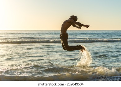 Healthy, fit and muscular black african american man jumping for joy on a beach during sunset while on vacation. Concept of a happiness, life and wellness