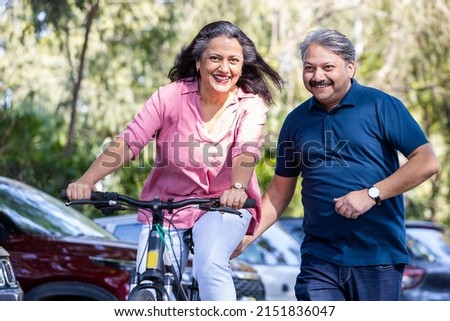 Healthy and fit old  Indian couple riding bicycle in the park summer, active old age people and lifestyle. Elderly woman learn to ride cycle with man. retired people having enjoy life. 