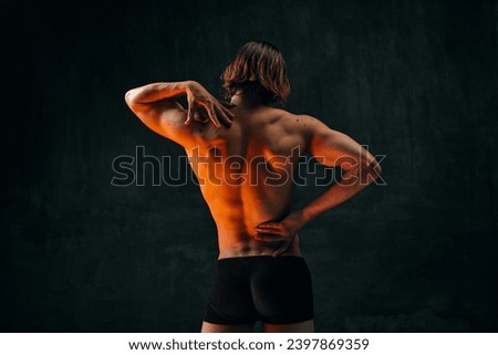 Healthy fit relief ack. Rear view of young shirtless man with muscular body standing in underwear against dark textured studio background. Concept of men's beauty, health, body art and aesthetics