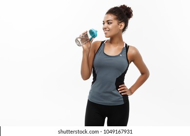 Healthy And Fitness Concept - Beautiful African American Girl In Sport Clothes Drinking Water After Workout. Isolated On White Studio Background