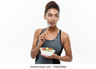 Healthy and Fitness concept - Beautiful American African lady in fitness cloth on diet eating fresh salad . Isolated on white background.