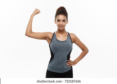 Healthy and Fitness concept - Portrait of young beautiful African American showing her strong muscle with confident cheerful facial expression. Isolated on white studio background. - Powered by Shutterstock