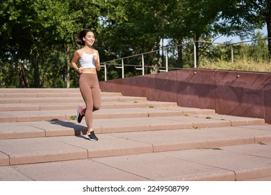 Healthy fitness girl running outdoors on street, wearing uniform, jogging on fresh air and listening music in wireless headphones. - Powered by Shutterstock