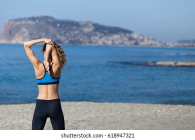 Healthy and fitness lifestyle Backview portrait of young woman wearing gym clothing stretching arms and exercising by seaside with sea and Alanya castle background Portrait layout.
