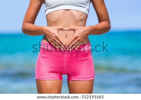 Healthy fitness woman with good stomach digestion. Hands forming heart shape. Body care, pregnancy, weight loss diet concept. Woman with intestine or reproduction problem.