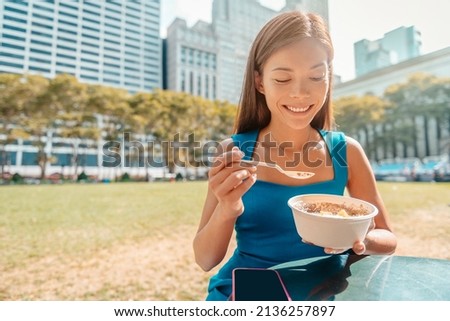 Healthy food Asian woman eating Acai bowl breakfast with spoon at New York City park on morning or lunch break. Businesswoman professional sitting outside summer lifestyle.